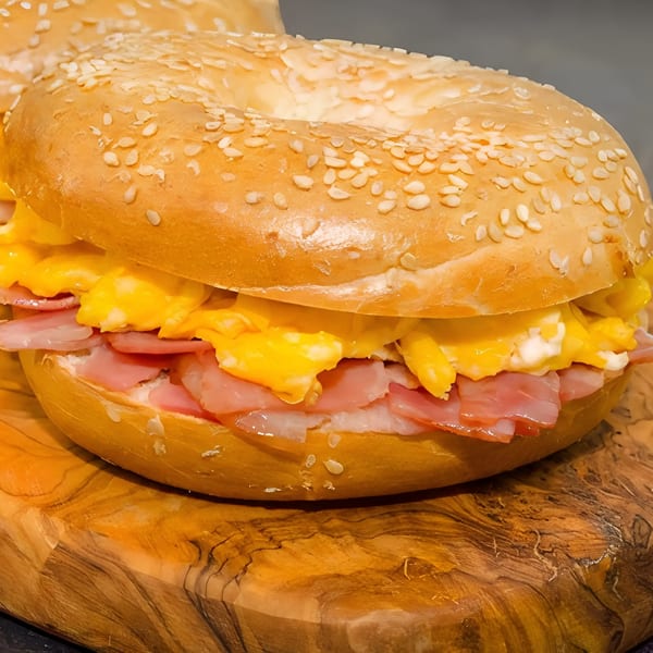 Close-up of a sesame bagel sandwich with scrambled eggs and ham on a wooden board.