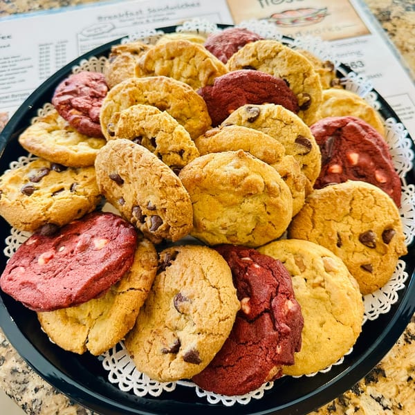 A black platter filled with an assortment of chocolate chip and red velvet cookies on white doilies.
