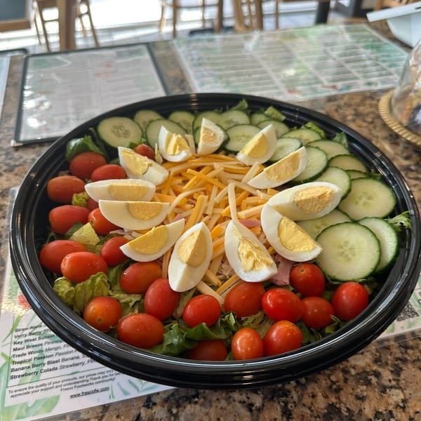 A large salad with lettuce, cherry tomatoes, cucumbers, shredded cheese, and sliced hard-boiled eggs.